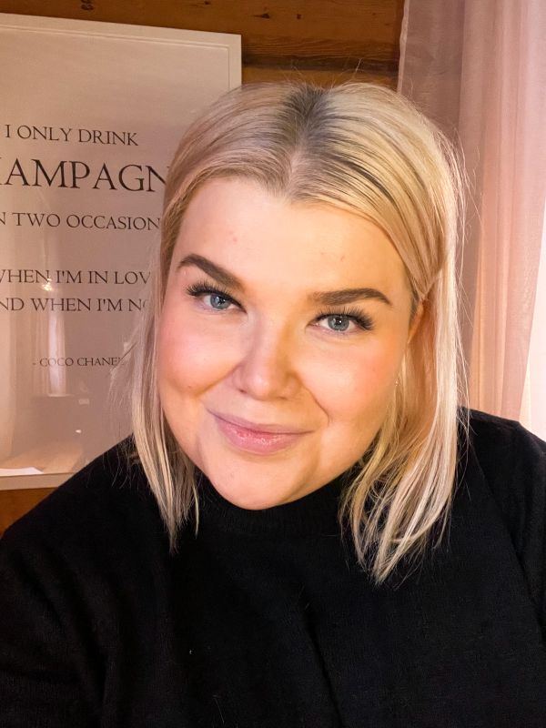 Emmillä on vaaleat hiukset ja musta paita. Hän hymyilee. 