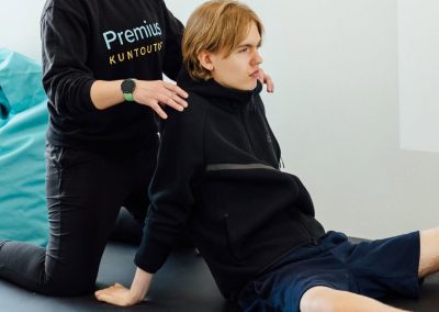 Fysioterapeutti ohjaa harjoittelijaa lattialla tehtävässä kuntoutusharjoituksessa vaaleassa kuntoutustilassa.