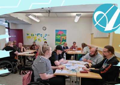 Ryhmä ihmisiä istuu pöytien ääressä keskustelemassa ja tekemässä ryhmätehtävää koulutus- tai työpajatilaisuudessa. Osallistujista osa käyttää pyörätuolia. Huoneen seinillä näkyy muistilappuja ja värikäs puuta esittävä juliste. Kuvan oikeassa yläkulmassa on Aksonin logo.